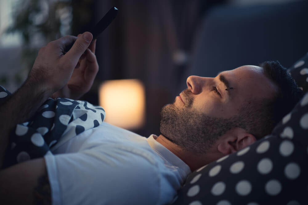 Man met smartphone in bed lijdt aan nomofobie