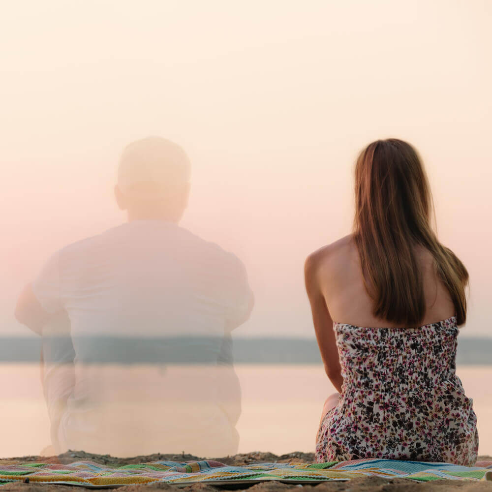 Vrouw die alleen zit op het strand met de gedachte van haar ex naast zich