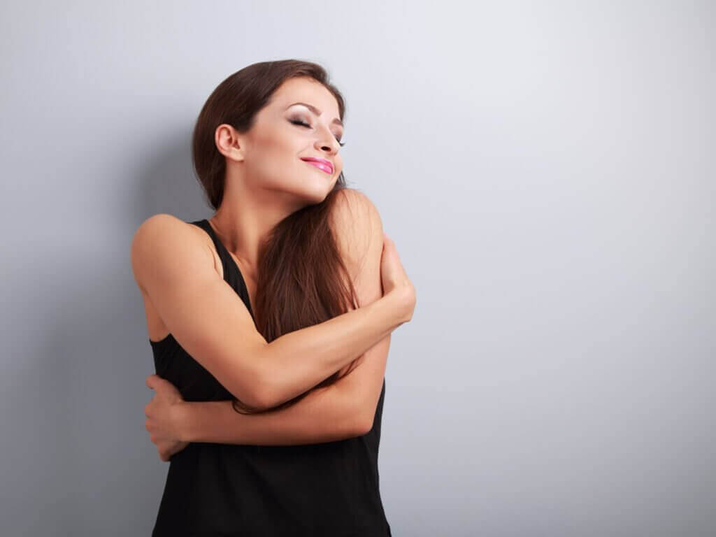 Vrouw omarmt zichzelf met een glimlach op haar gezicht