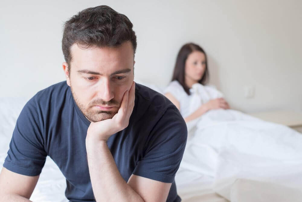 Vrouw ligt op bed en man zit zwaarmoedig op het randje van het bed
