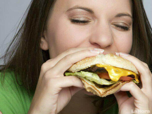 Vrouw eet met gesloten ogen een hamburger