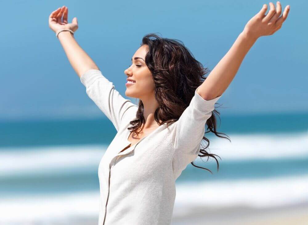 Vrouw staat met gespreide armen bij de zee