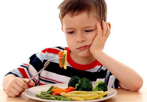 Een kind met groenten op zijn vork en een ontevreden uitdrukking