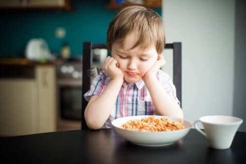 Jongen zit bij zijn bord eten te mokken