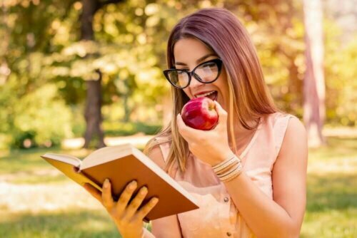 Een vrouw leest een boek terwijl ze een appel eet
