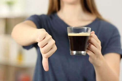 Een vrouw houdt een kop koffie in haar hand en doet haar duim omlaag