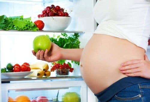 Zwangere vrouw staat bij allerlei groente en fruit