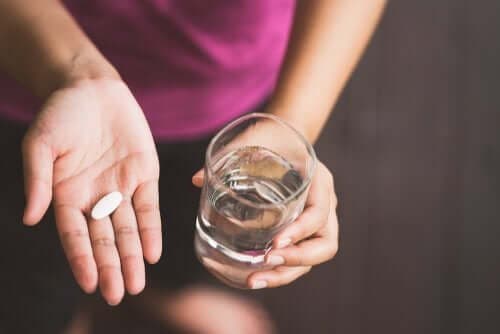Een vrouw heeft een pil en een glas water in haar handen