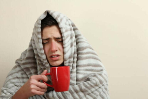 Een man zit onder een deken met een kop thee