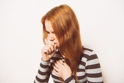 Een vrouw hoest en houdt haar hand voor haar mond