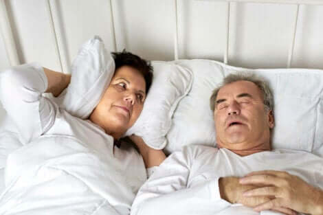 Een man snurkt in bed en zijn vrouw houdt een kussen tegen haar oren