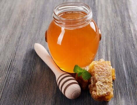 Een pot honing met een stukje honingraat ernaast