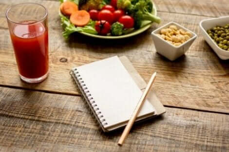 Een glas tomatensap met een gezonde salade en een opschrijfboekje op tafel