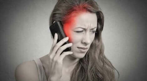 Een vrouw met hoofdpijn die haar mobiele telefoon vasthoudt