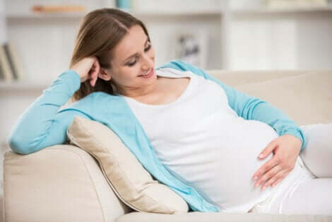 Een zwangere vrouw lacht terwijl ze haar buik aanraakt