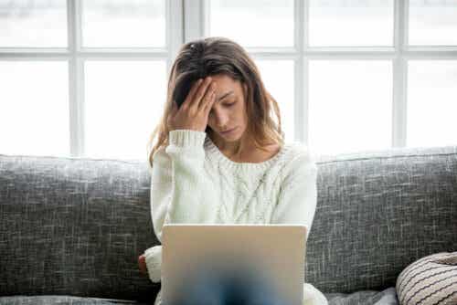 Een vrouw met haar hand tegen haar hoofd zit achter een laptop