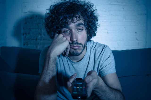 Een man die zich verveelt terwijl hij in het donker tv kijkt