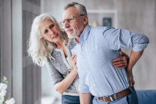 Een oudere vrouw houdt een oudere man overeind, die naar zijn rug grijpt