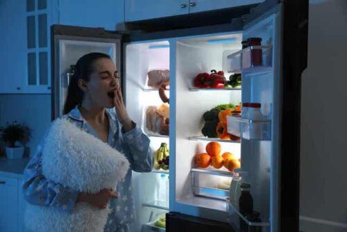 Een vrouw gaapt en staat voor de koelkast