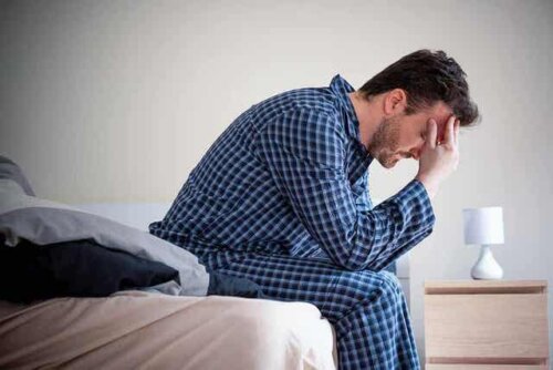 Een man zit op de rand van zijn bed met zijn hoofd in zijn handen