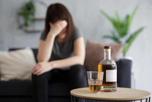 Een vrouw zit met haar hand tegen haar hoofd en een fles alcohol op de voorgrond